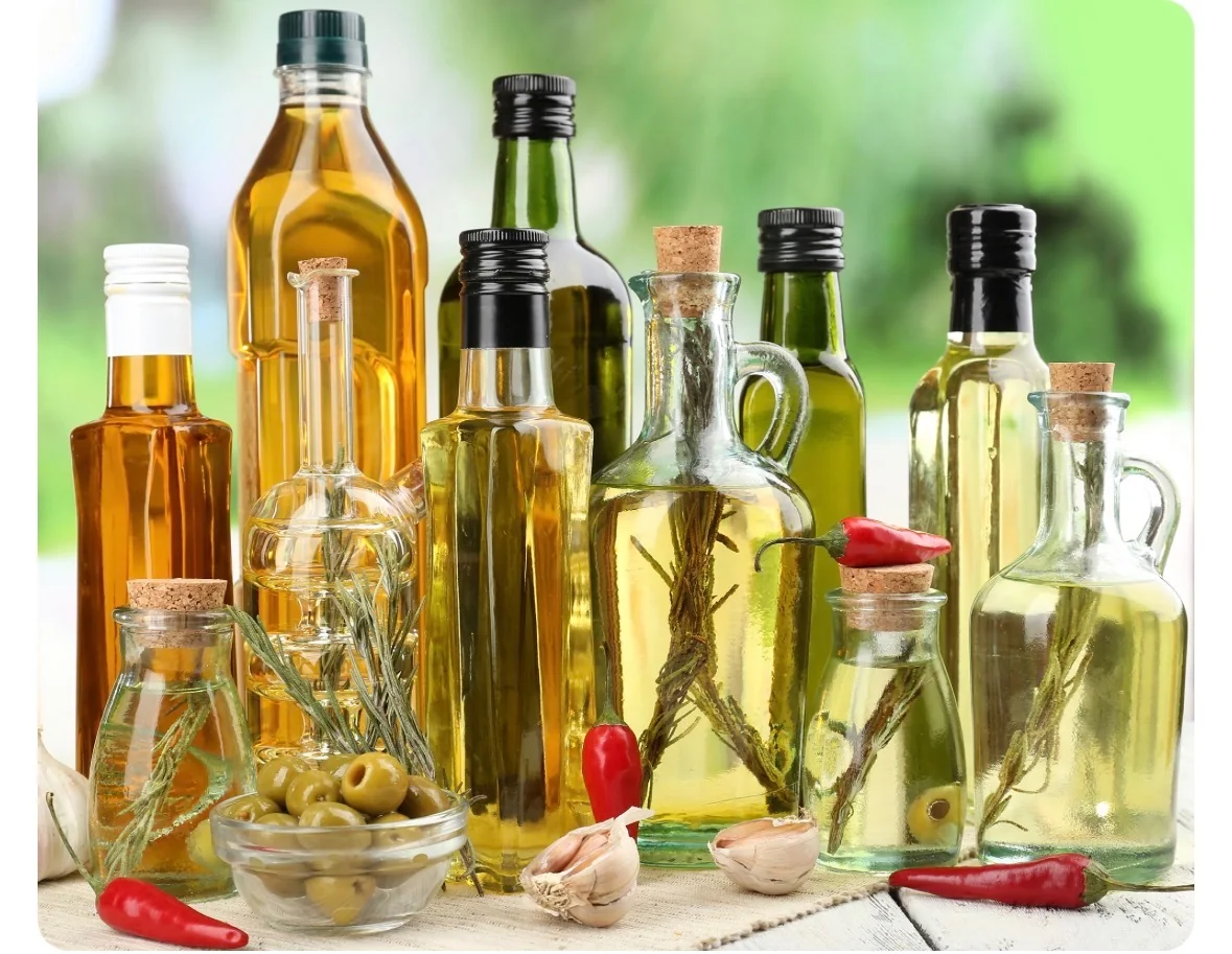Assorted glass bottles and cruets of edible oils with rosemary sprigs, olives, garlic and red chillies on a wooden table